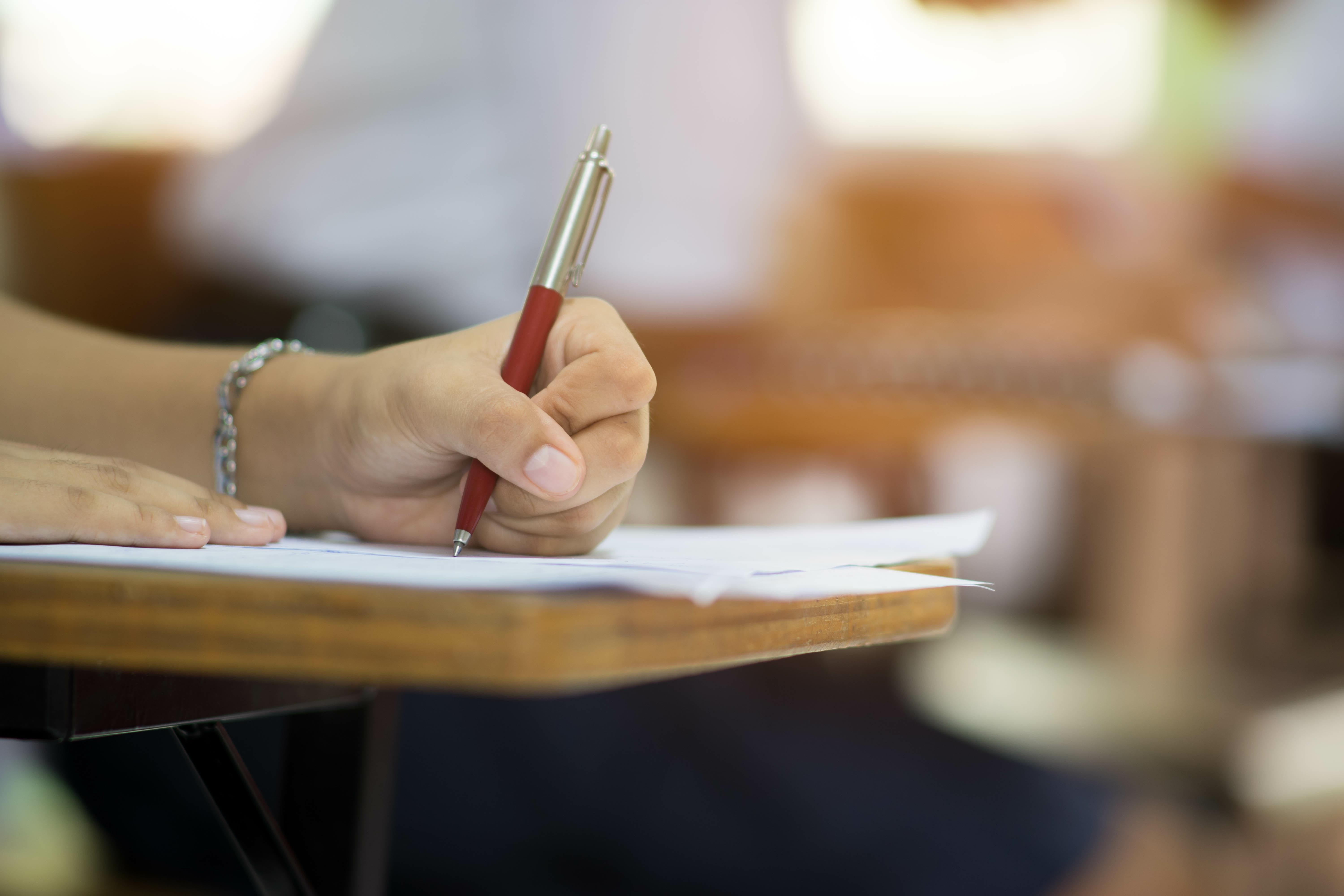 Closeup to hand of student holding pen and taking exam in cl