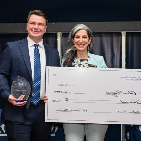 A man holds an award and a woman holds a large-format check for $10,000.