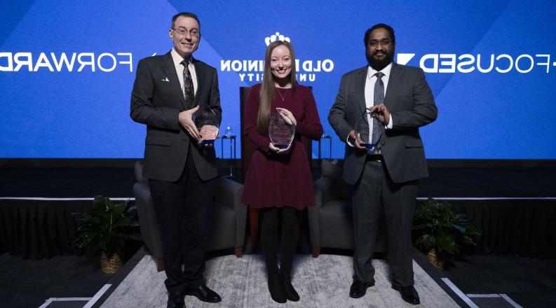 Three people holding awards in front of a screen that reads "forward-focused" 